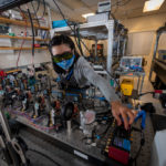 <p>Early Career Research Scientist Dan Wang working on the piezo inertia motor controllers to drive piezo mirrors, for laser alignment in the coherent laser combining system. (Credit: Thor Swift/Berkeley Lab)</p>
 